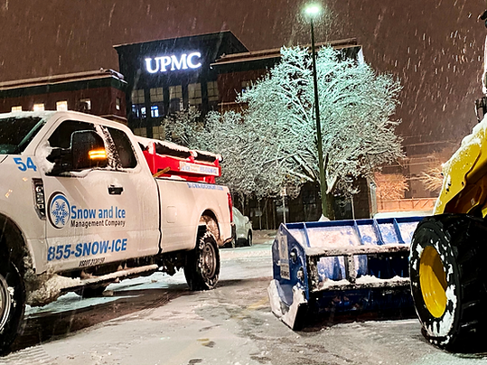 Snow plow and front loader in snow covered parking lot during winter storm